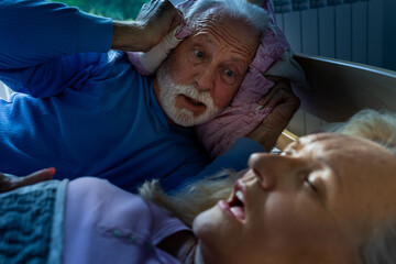 Woman snoring in bed while husband holding pillow on ears