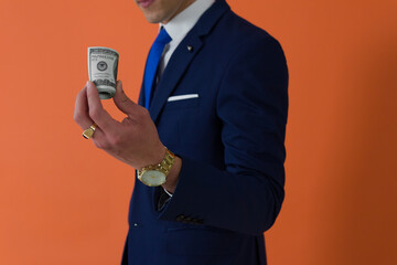 cut-out shot of a dapper anonymous man dressed in suit holding a wad of dollars ahead an orange background
