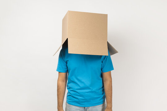 Portrait of unknown anonymous man wearing blue T- shirt standing with cardboard box on his head, having fun, hiding his face in carton parcel. Indoor studio shot isolated on gray background.