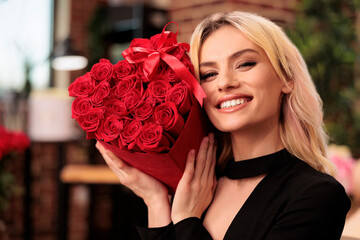 Girlfriend holding red roses bouquet celebrating love holiday, standing in living room filled with...