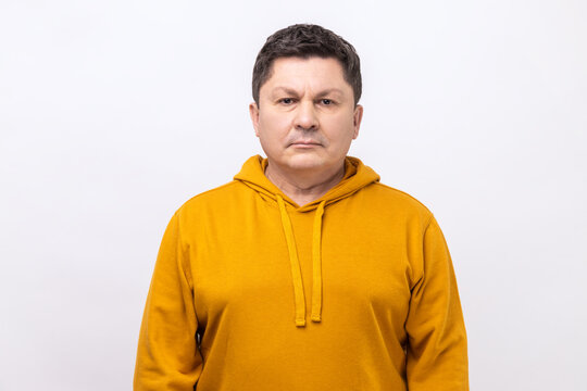 Portrait of serious self assured unsmiling man with dark hair seriously looking at camera, confidence, wearing urban style hoodie. Indoor studio shot isolated on white background.