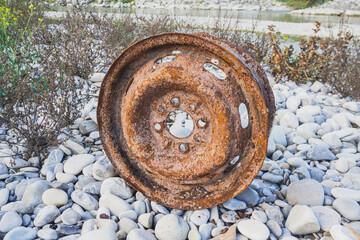 Old car wheel, rusty car alloy rim on stones by the river