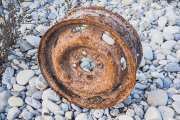 Old car wheel, rusty car alloy rim on stones by the river