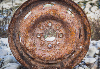Old car wheel, rusty car alloy rim on stones by the river