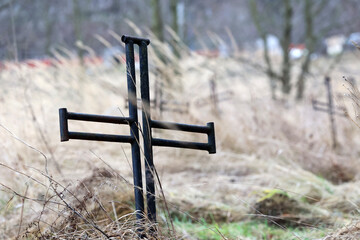 Stary  zardzewiały stalowy krzyż na cmentarzu wojennym. Krzaki.  - obrazy, fototapety, plakaty