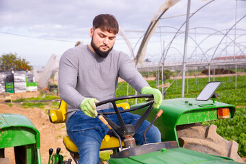 Skillful bearded guy driving farm tractor during spring works on his vegetable garden