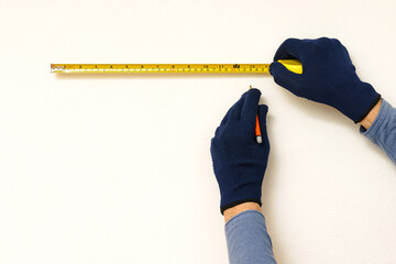 Builder's hands with measuring tape and pencil on white wall. Close up.