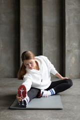 Fototapeta na wymiar An athlete in leggings, a hoodie and sneakers stretches the muscles of her legs before training