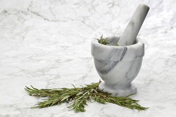 Rosemary herbs and a mortar and pestle on grey and white marble surface