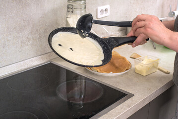 woman cook pours pancake dough into a hot pan over the stove.