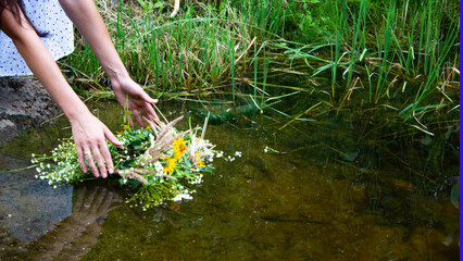 The girl's hands lower a wreath of flowers into the river. On the feast of Ivan Kupala girl weaves a wreath of flowers and sends the wreath to float on the river. Slavic traditions. © Volha