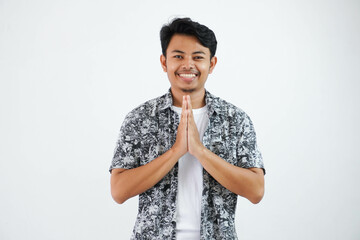 smiling young asian man both hands together over his chest, expressing respect and grateful standing looking camera isolated on white background