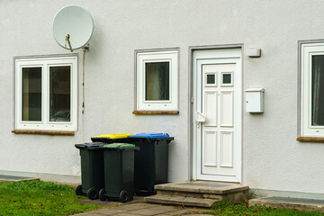 Plastic trash cans near the entrance to a residential building. Satellite dish on the wall above...