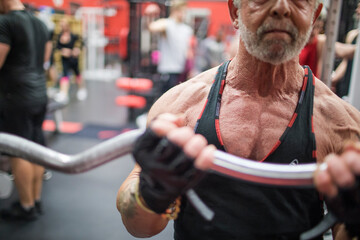 Fit elderly man training his biceps at the gym.