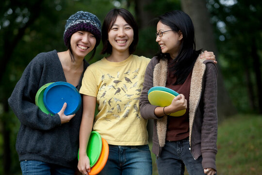 Portrait of three young Asian-American woman playing flying disk golf in Baltimore, Maryland.