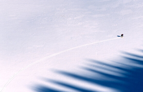 Man skiing across flats in a tuck with shadows of trees.