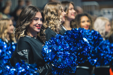 Medium shot of a group of cheerleaders cheering and holding blue pom-poms. Sport concept. High...