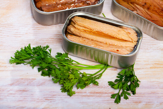 Open can of preserved natural fillet of frigate tuna on wooden table with fresh parsley ..