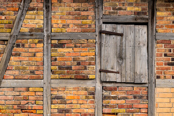 Weathered timber frame wall background, with bleached wooden beams, red brick stones and a small wooden door