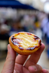 Hand with Portugal's traditional sweet dessert Pastel de nata egg custard tart pastry and view on street in Lisbon, Portugal