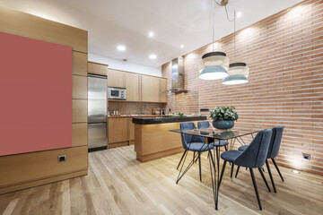 Studio apartment with open kitchen with polished black granite countertops, brick wall, glass dining table with blue chairs, and oak hardwood floors