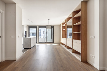 Living room of an empty house with custom-made oak bookcase, open kitchen on one side and terrace...