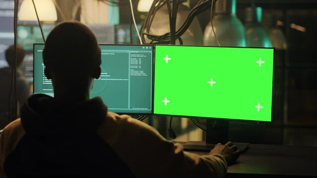 Male hacker using greenscreen display to hack online server, planning phishing attack late at night. Young man doing illegal activity with isolated chroma key template and copyspace, security breach.
