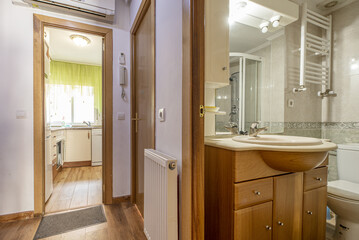 Bathroom with wooden bathroom cabinet with drawers and doors, marble countertop and mirror with wall sconces next to a corridor with access to other rooms