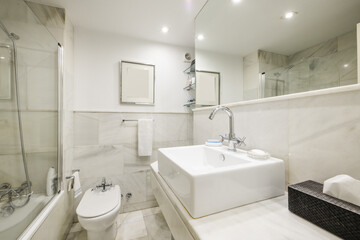 Beautiful bathroom with white marble tiles with a mirror integrated into the wall, an educational cabin with a glass partition and porcelain toilets