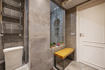 Shower cabin of a bathroom with light slate tiling, wooden plank seat and chrome metal radiator
