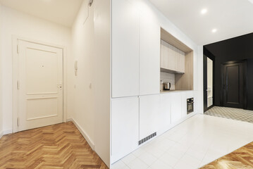 Entrance hall of a loft-style vacation rental home with a kitchen open to the living room with white cabinets combined with oak wood surfaces