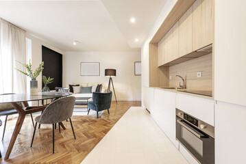 Loft-style vacation rental home with an open kitchen to the living room with white cabinets paired with oak wood surfaces and a black glass dining table with gray velvet chairs