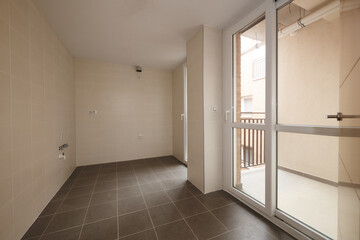 Empty room to install a kitchen with a clothesline terrace with a white aluminum door and screen and dark stoneware floors