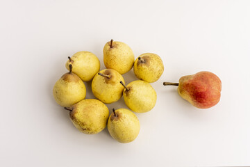 A bunch of yellow and one red pears on a white smooth surface