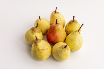 A bunch of yellow pears with their stems upright and a red one in the center on a white smooth surface