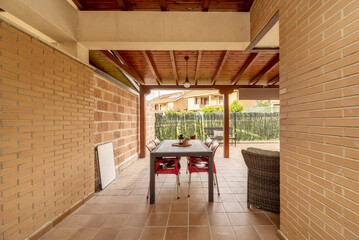 Patio of a detached house with light brown stoneware floors, exposed brick walls, lawned gardens and a porch made of varnished pine logs