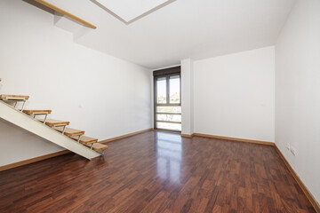 Empty room of a two-story loft with a white metal staircase and wooden steps, jatoba wood flooring and a bay window in one corner