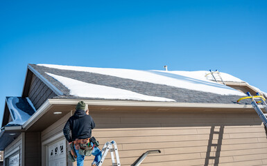 Contractor installing gutters on a residential building in the winter with snow on the roof.