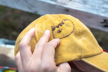 Female hand-holding yellow embroidery hat and needle working on cat pattern stitching in a process...