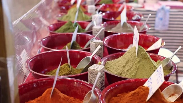 Oriental powdered spices of different varieties and colors in red clay plates lie in two rows on the counter in the store, side view close-up with a smooth zoom forward.Spice shopping concept.