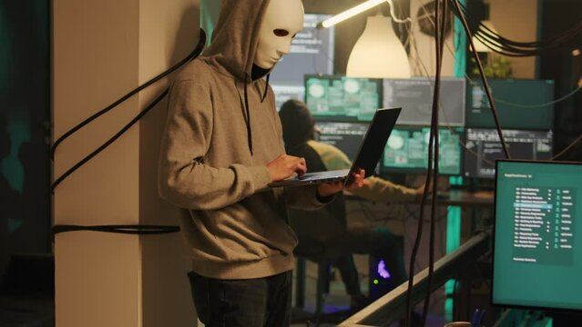 Thieves with anonymous masks hacking computer to steal information directly from government system, cybercrime. Masked cyber criminals using malware to break into online software.