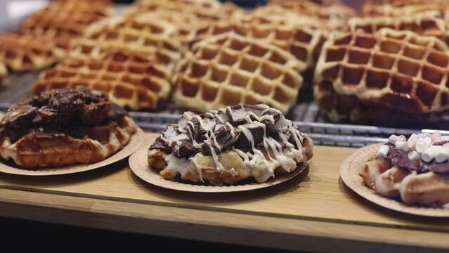 Appetizing Belgian waffles with chocolate and caramel filling with cream in craft disposable plates lie on the counter in the store, close-up side view with a smooth circular zoom. Waffle shopping con