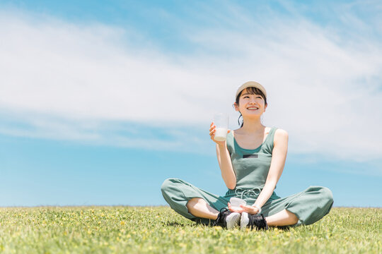 青空のもと公園でプロテイン・牛乳・豆乳を飲むアジア人女性