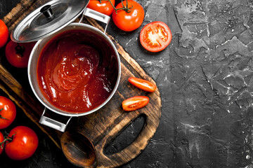 Tomato sauce in a pot on a cutting Board and tomato slices.