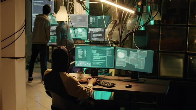 Young cyber criminal breaking computer firewall to plant malware for dos, stealing government data on multi monitors. Male hacker using network malware to hack online espionage system.