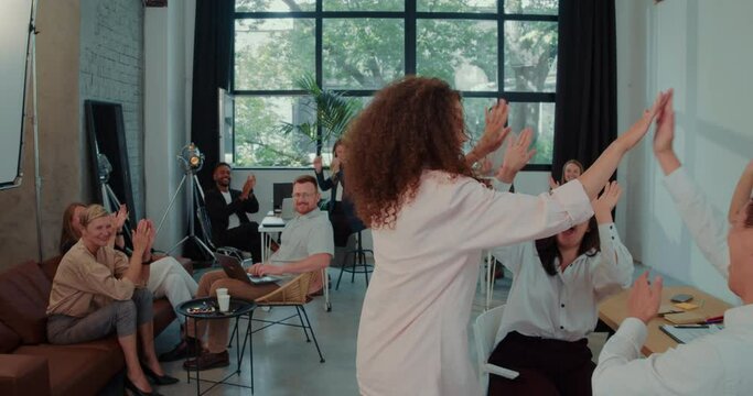 CELEBRATING SUCCESS Excited young mixed race female startup founder enter office dancing welcomed by team slow motion.