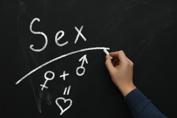 Sexual education. Man underlining word Sex on black chalkboard, closeup. Chalked heart, female and male gender signs