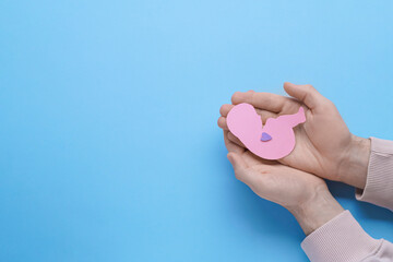 Female health. Man holding newborn paper figure on light blue background, top view with space for text