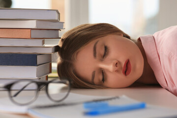 Young tired woman sleeping near books at white table indoors, closeup