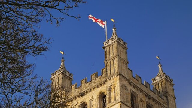 English flag flying proudly from the top of a tower against a brilliant blue sky.